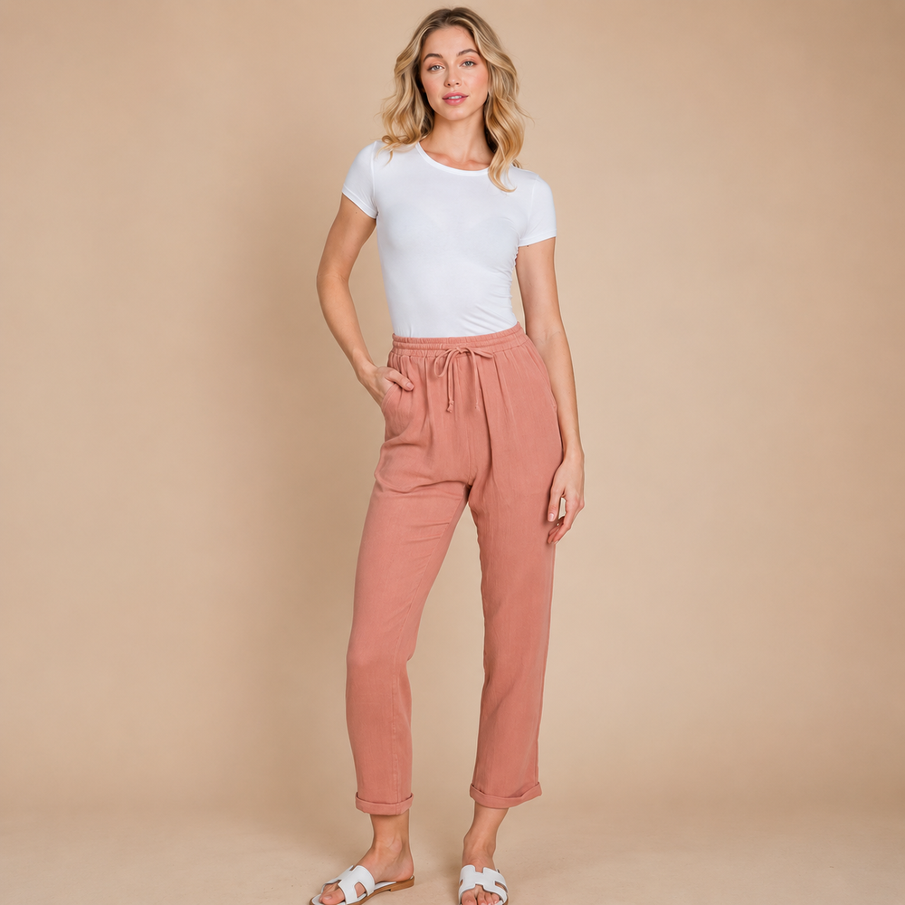 Woman wearing a white t-shirt and pink pants against a beige background