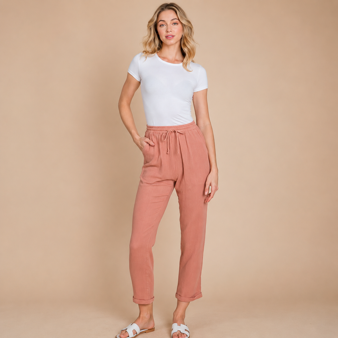 Woman wearing a white t-shirt and pink pants against a beige background
