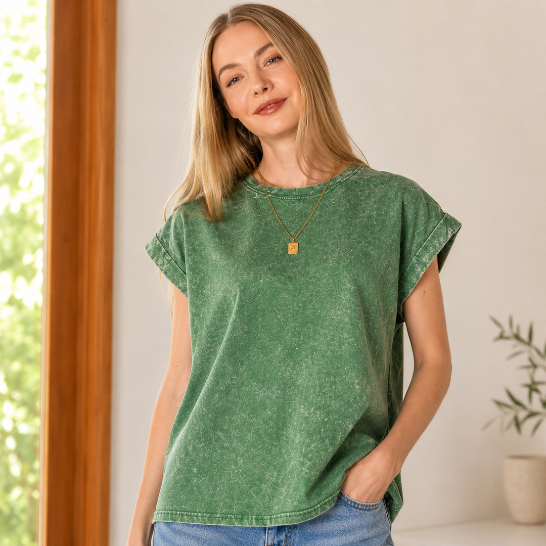 Woman wearing a green t-shirt and blue jeans indoors with a neutral background