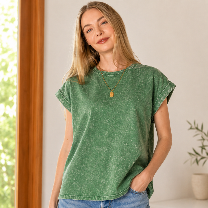 Woman wearing a green t-shirt and blue jeans indoors with a neutral background