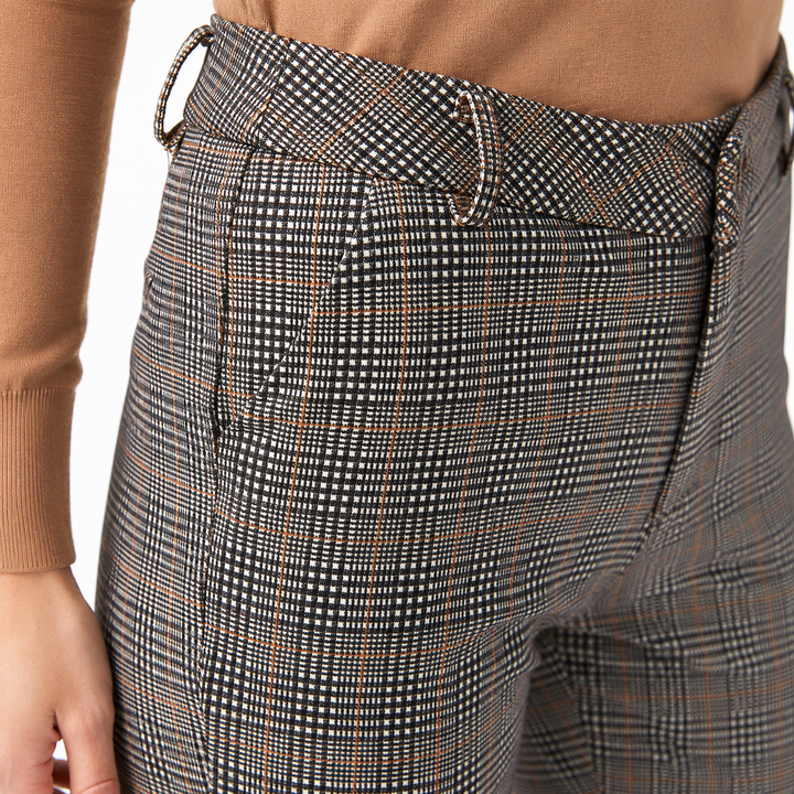 Close-up of a person wearing high-waisted plaid trousers with a brown ribbed long-sleeve top, showing the waistband, belt loops, front pocket, and fabric pattern against a white background.