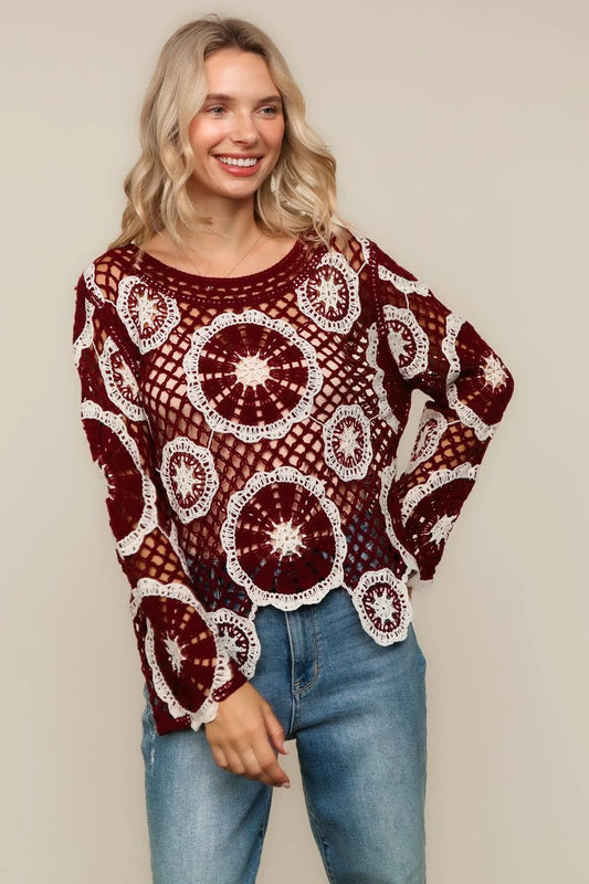 Woman wearing a burgundy and white patterned sweater with blue jeans on a beige background