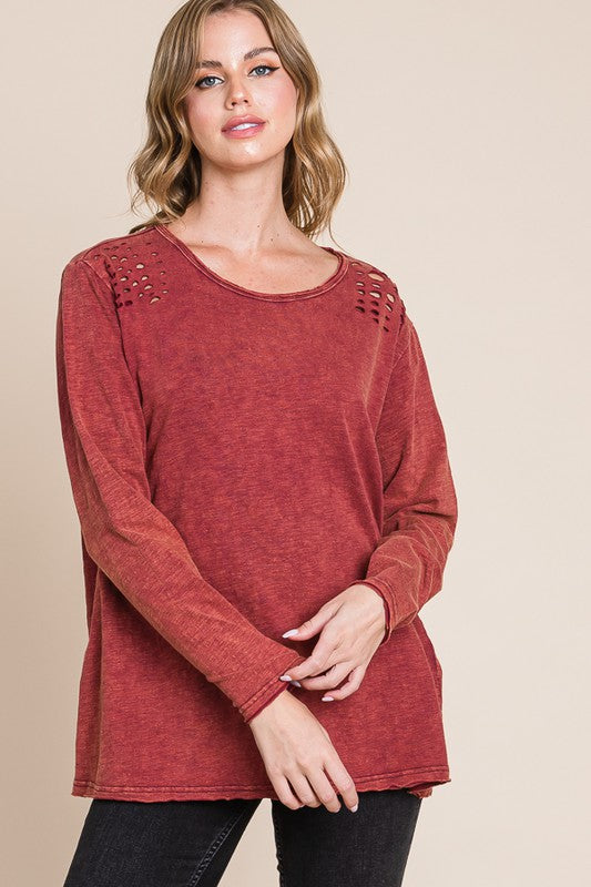 Woman wearing a red long-sleeve top with cut-out shoulders against a beige background