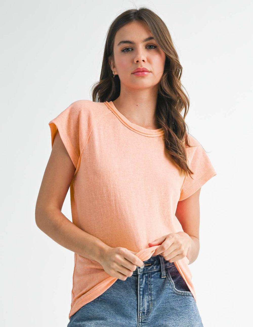 Woman wearing a peach-colored top and denim shorts on a white background