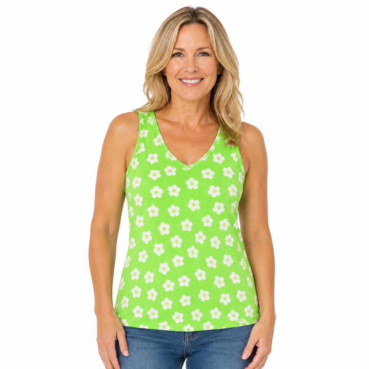 A smiling blonde woman wearing a bright lime green sleeveless tank top with a white daisy pattern, paired with blue jeans, against a plain white background.