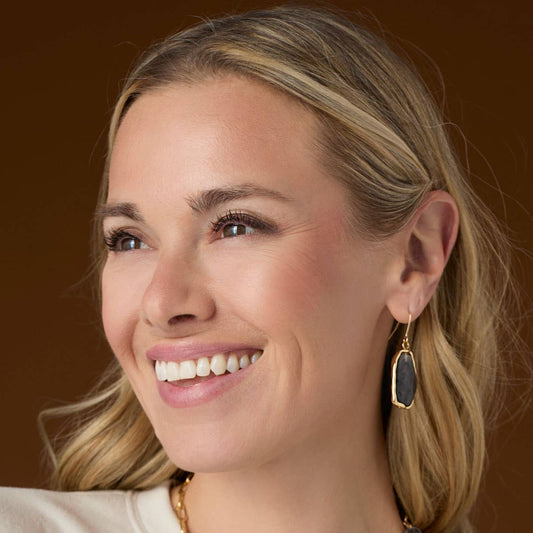 Close-up of a woman wearing gold earrings with a brown background