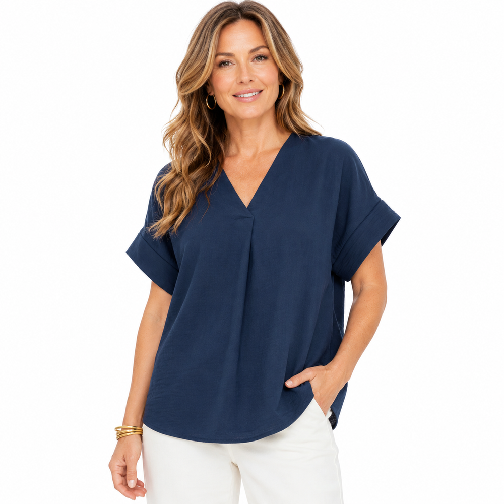 A woman modeling a navy blue short-sleeve V-neck blouse with a gathered front detail, paired with white pants, against a solid white background.