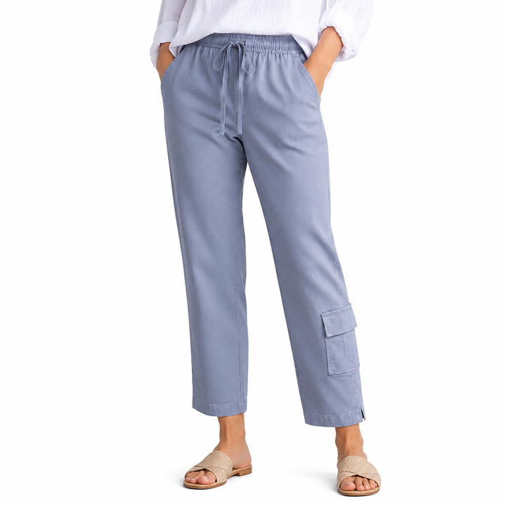 A person wearing light blue cropped drawstring pants with side cargo pockets, paired with a white blouse and beige slide sandals, shown against a plain white studio background.