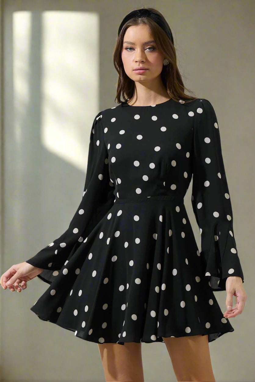 Black dress with white polka dots worn by a model on a plain background