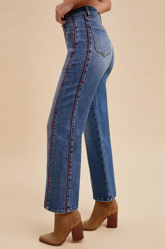 Blue jeans with red stitching worn by a person on a beige background