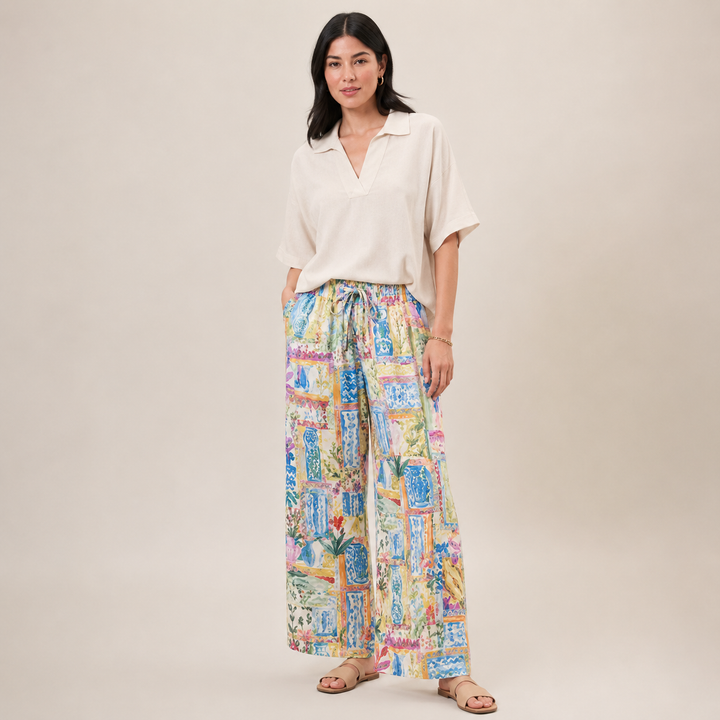 Woman wearing a white blouse and colorful patterned pants on a beige background
