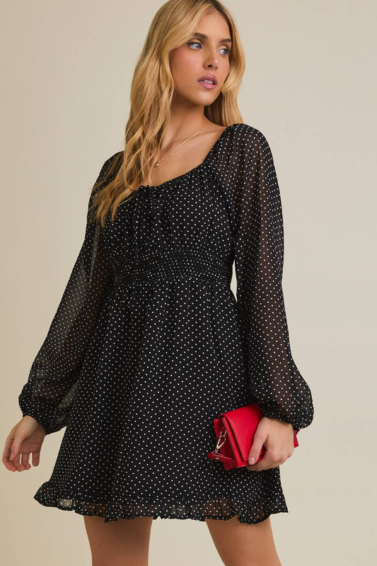 Woman wearing a black polka dot dress with long sleeves against a beige background
