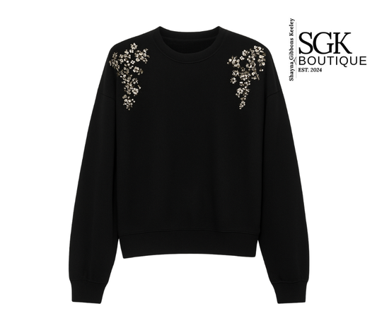 Black sweatshirt with floral embellishments on shoulders by SGK Boutique.
