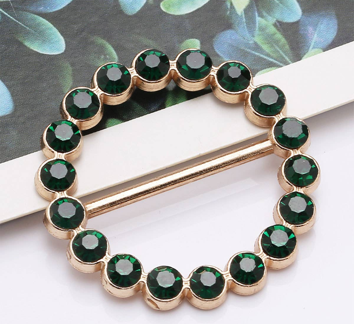 Gold brooch with green gemstones on a white surface
