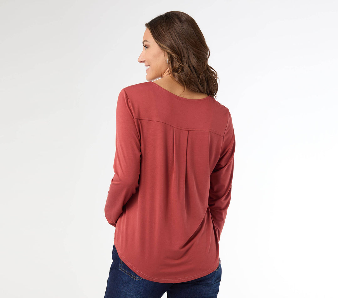 Woman wearing a burnt orange long-sleeve top and blue jeans on a white background