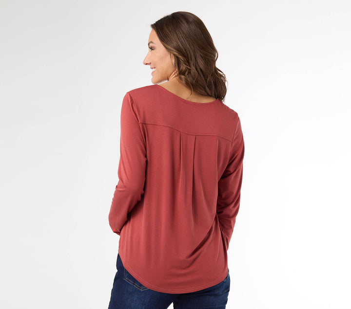 Woman wearing a burnt orange long-sleeve top and blue jeans on a white background