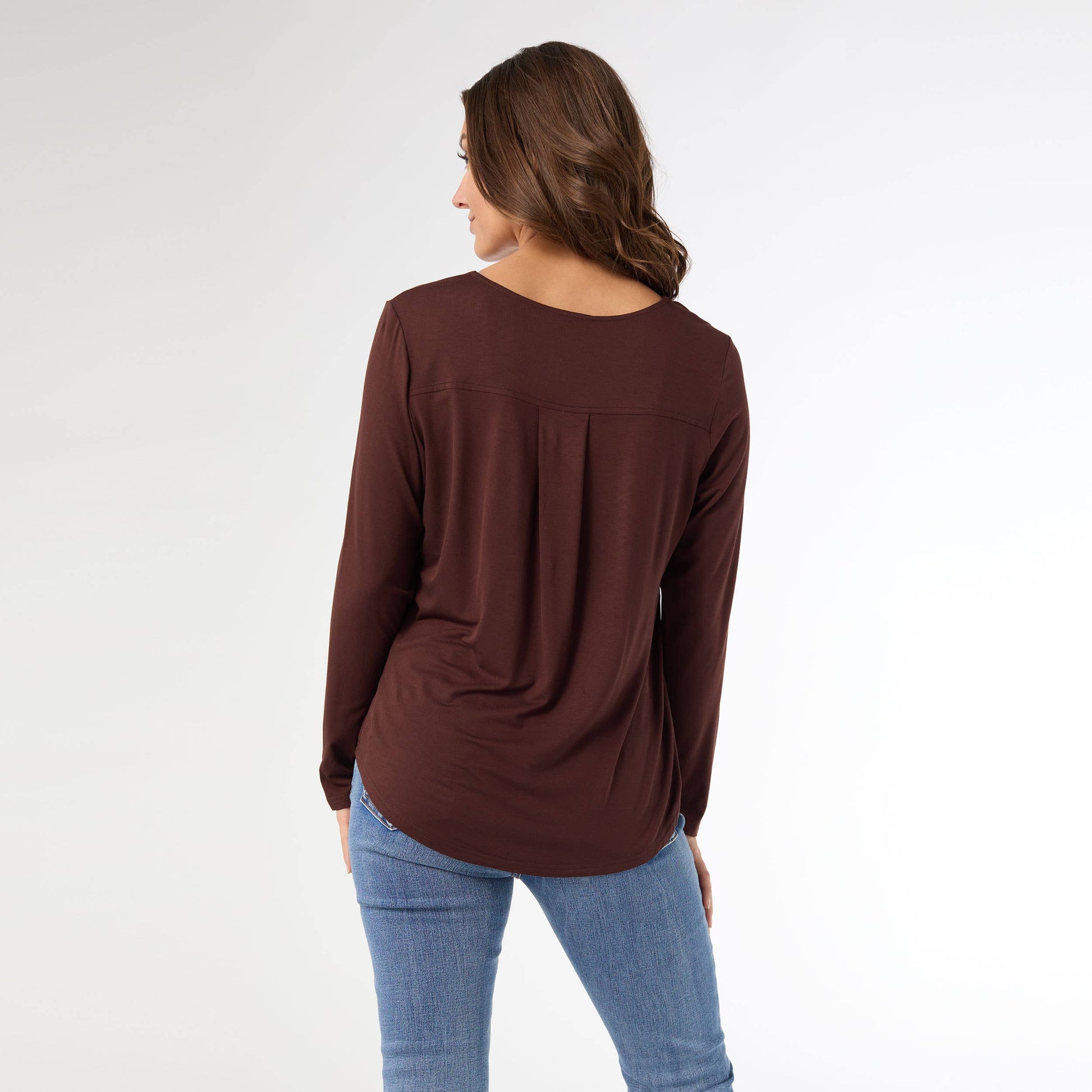 Woman wearing a brown long-sleeve top and blue jeans on a white background