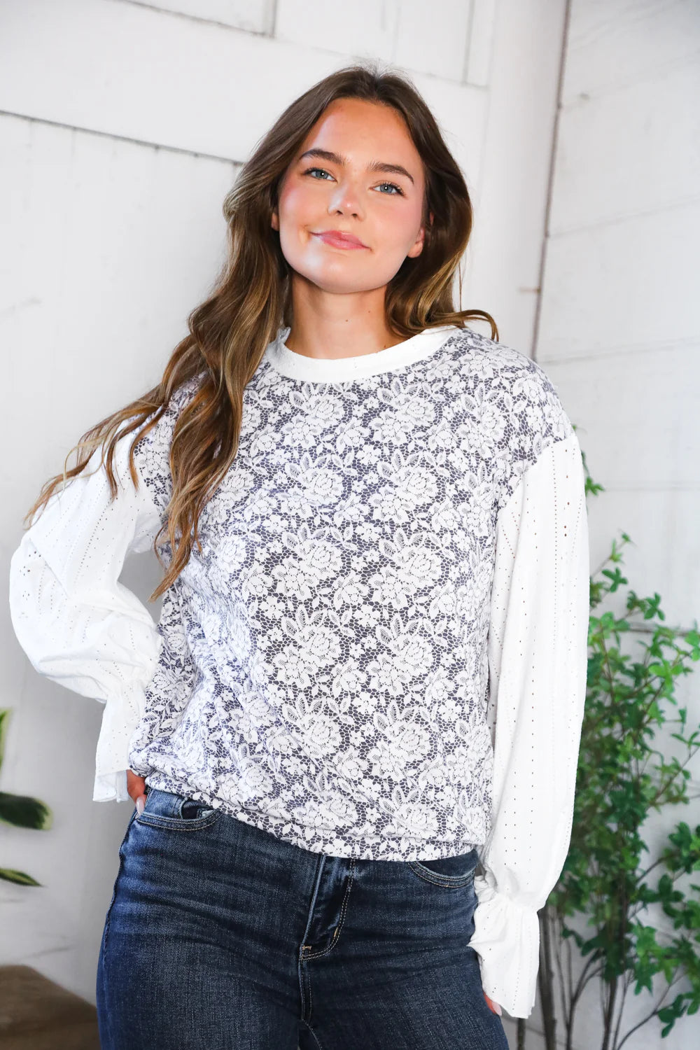 Woman wearing a white floral blouse with long sleeves against a white wall.
