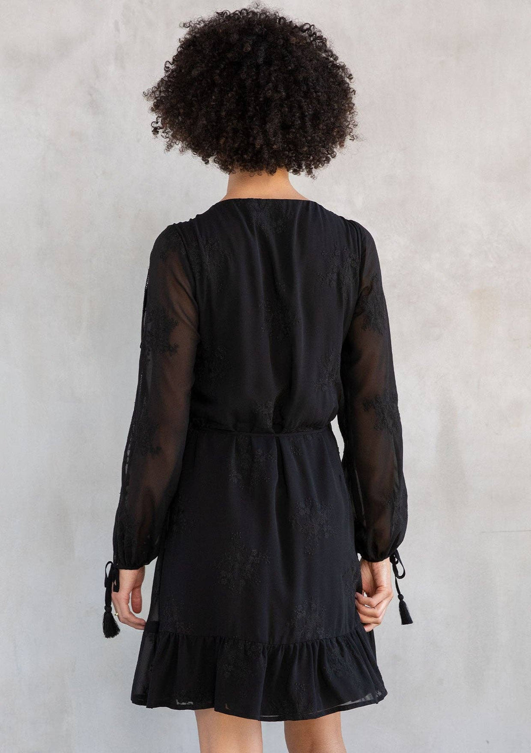 Person wearing a black dress with sheer sleeves against a plain background