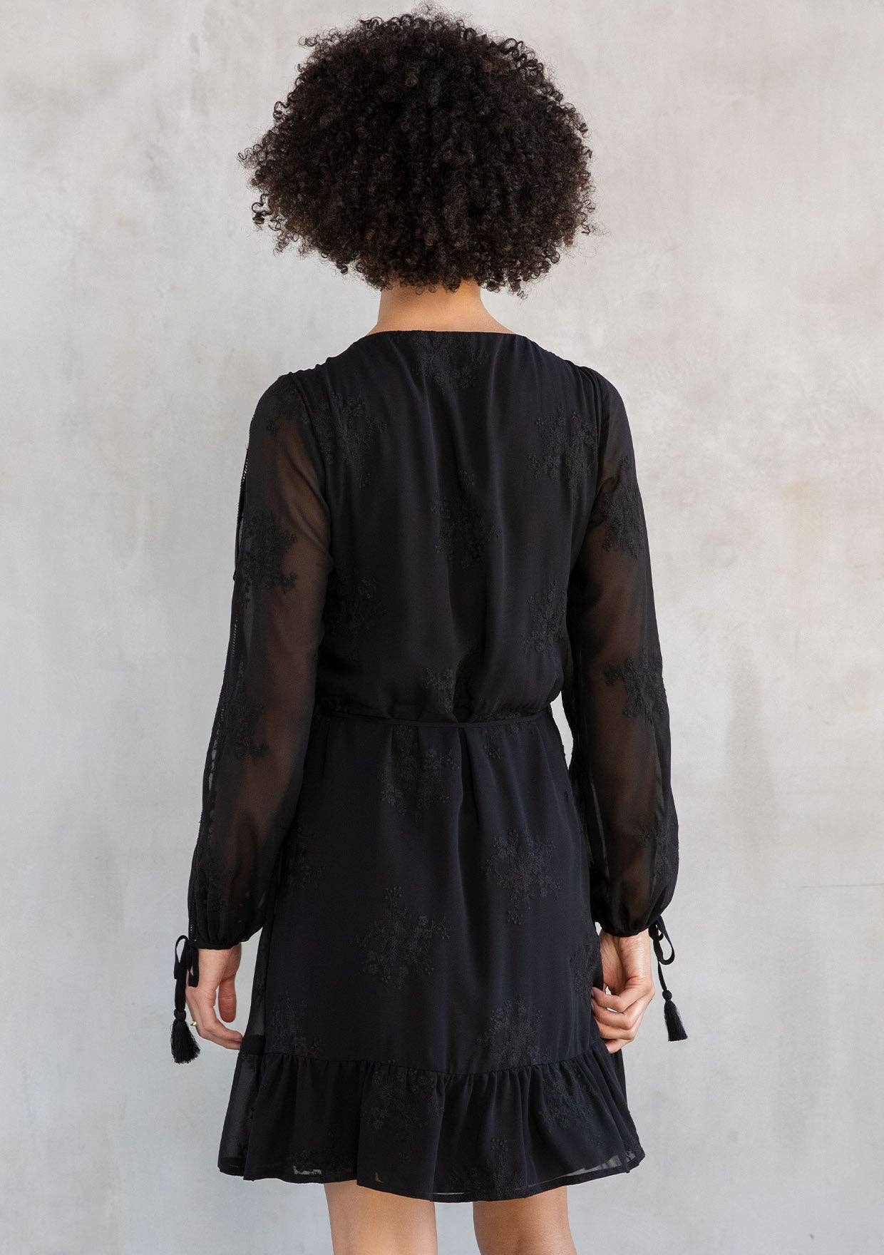 Person wearing a black dress with sheer sleeves against a plain background
