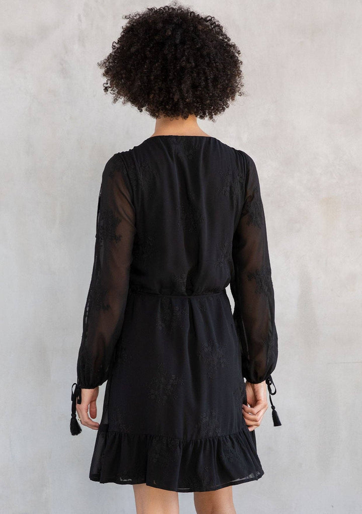 Person wearing a black dress with sheer sleeves against a plain background