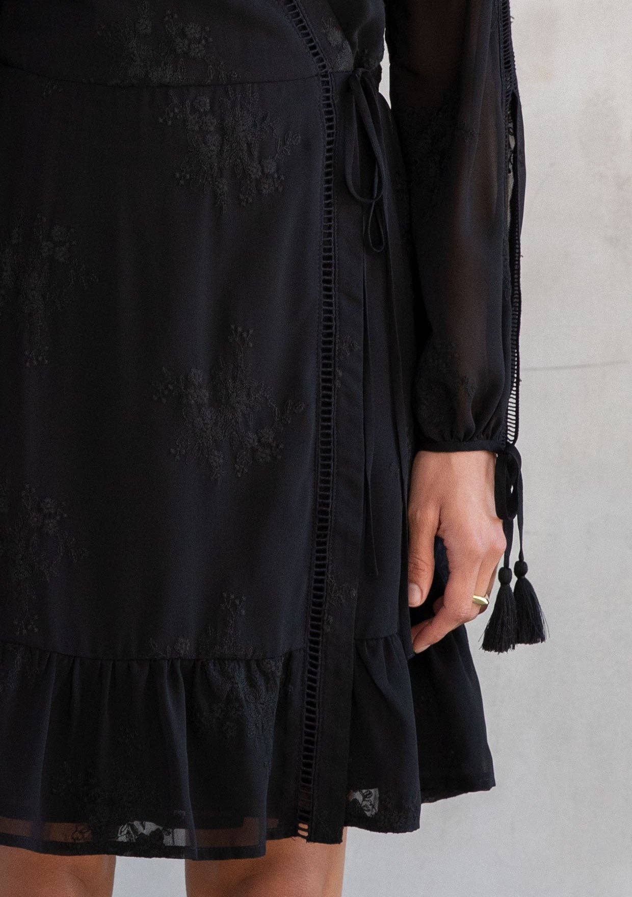 Black dress with lace details and tassels on a plain background