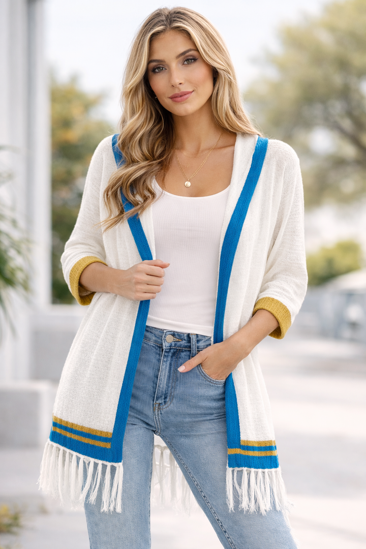 Woman wearing a white cardigan with blue and yellow trim, standing outdoors.