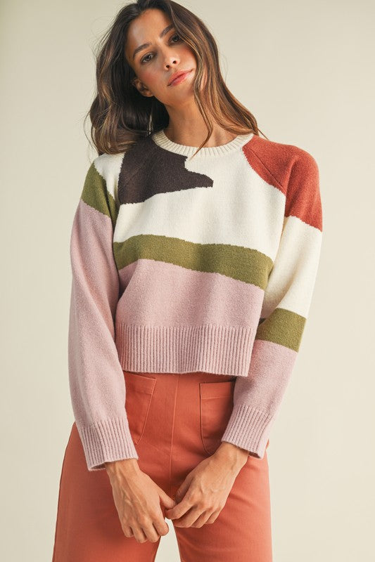 Woman wearing a colorful striped sweater and pink pants against a plain background