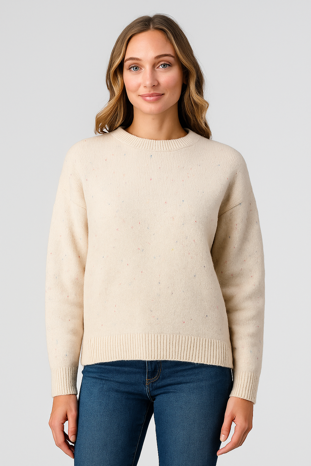 Woman wearing a beige sweater and blue jeans on a light gray background