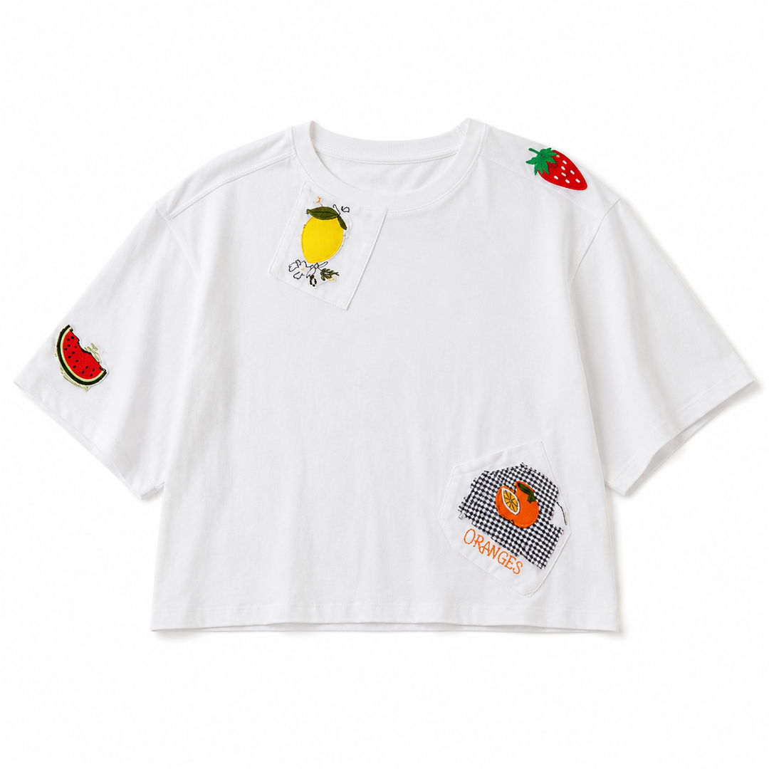 A white short-sleeve crop top T-shirt featuring colorful fruit-themed patchwork details on the chest, sleeves, and lower front, displayed flat against a clean white background.