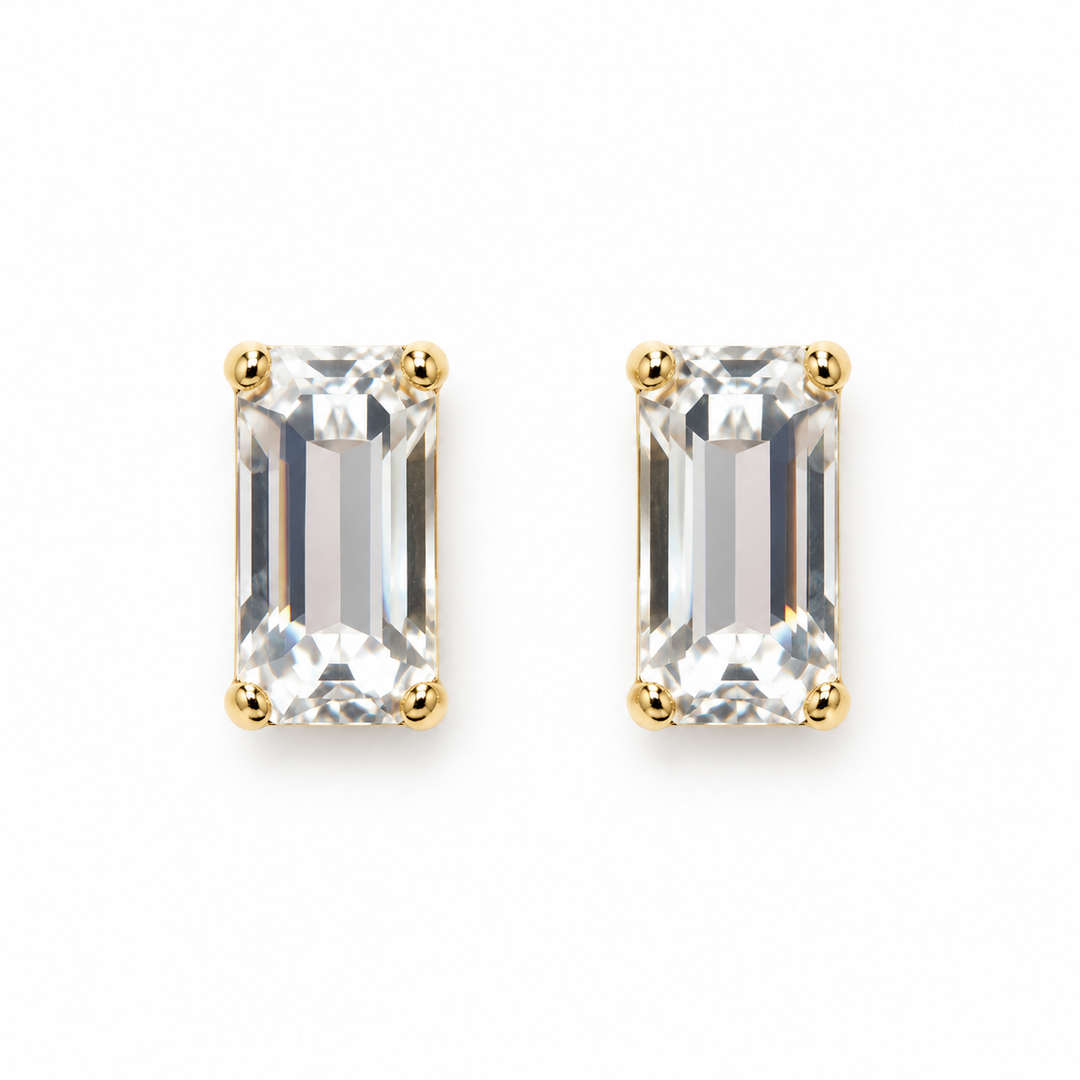 A pair of gold stud earrings featuring rectangular emerald-cut clear gemstones in four-prong settings, shown on a plain white background.
