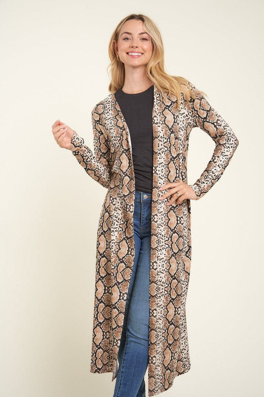 Woman wearing a snake print duster over a black top and blue jeans on a beige background