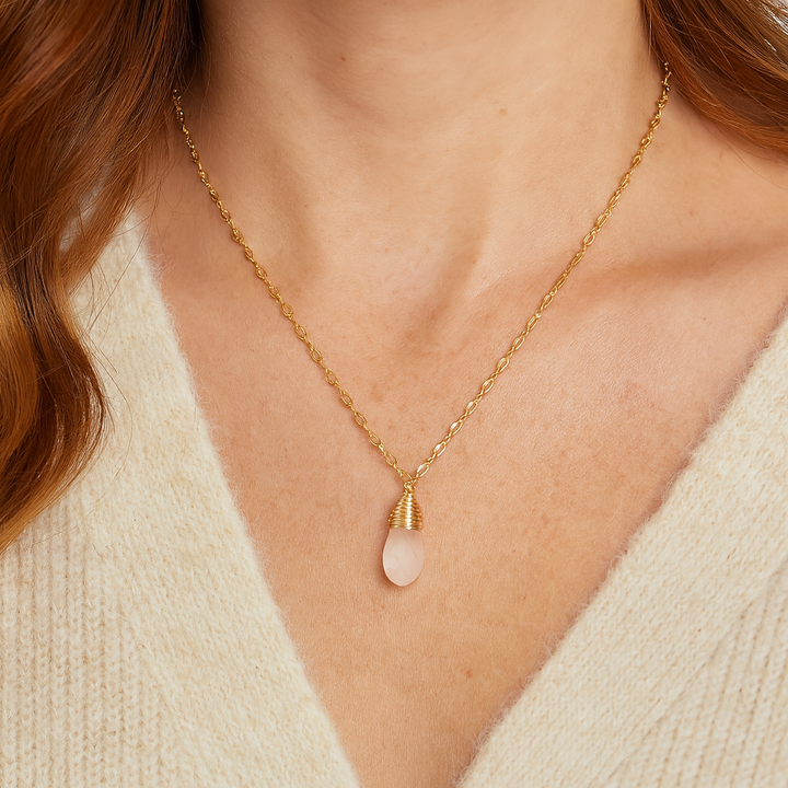 Gold necklace with a clear stone pendant on a person wearing a beige sweater.