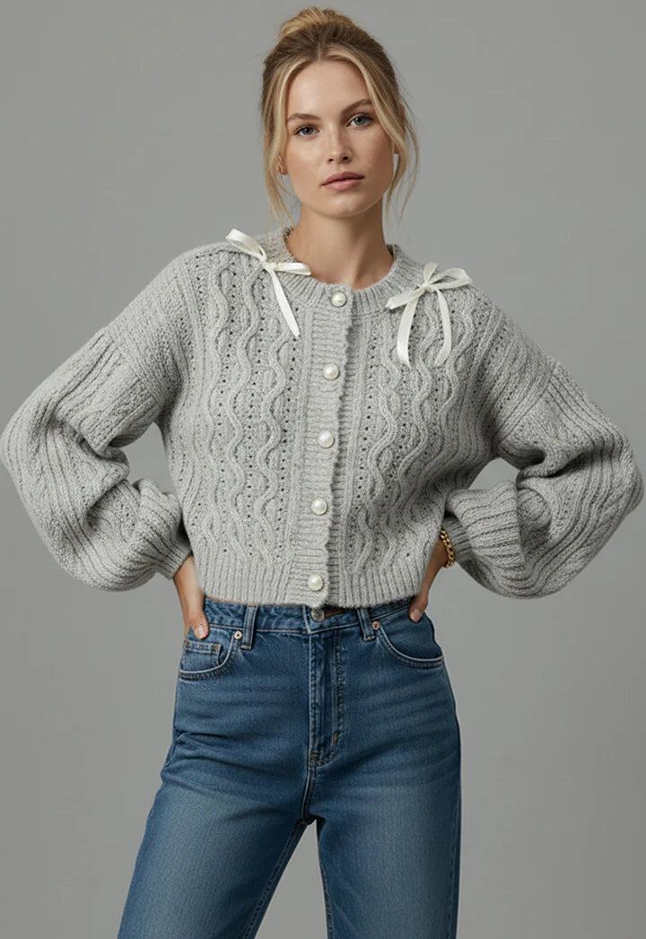 Woman wearing a gray cable knit sweater and blue jeans against a gray background
