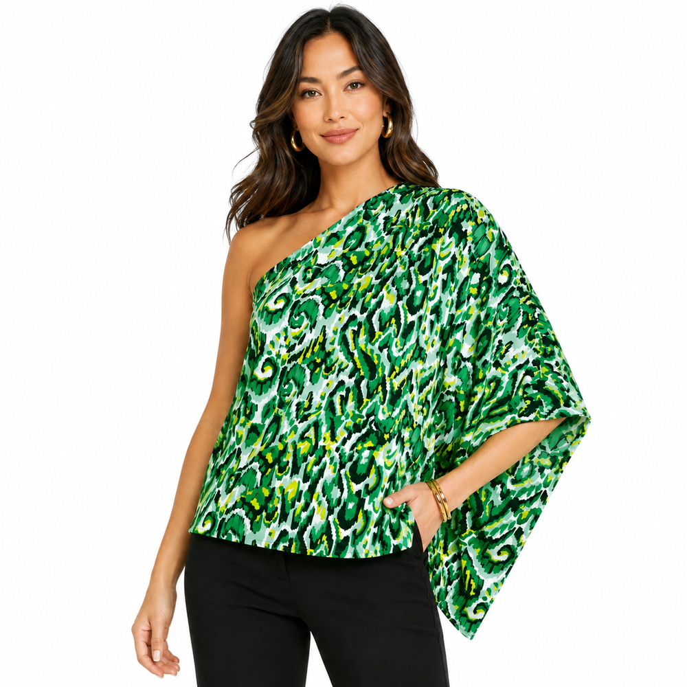 A woman modeling a green and white abstract-patterned one-shoulder top with wide draped sleeves, paired with black pants, against a plain white background.