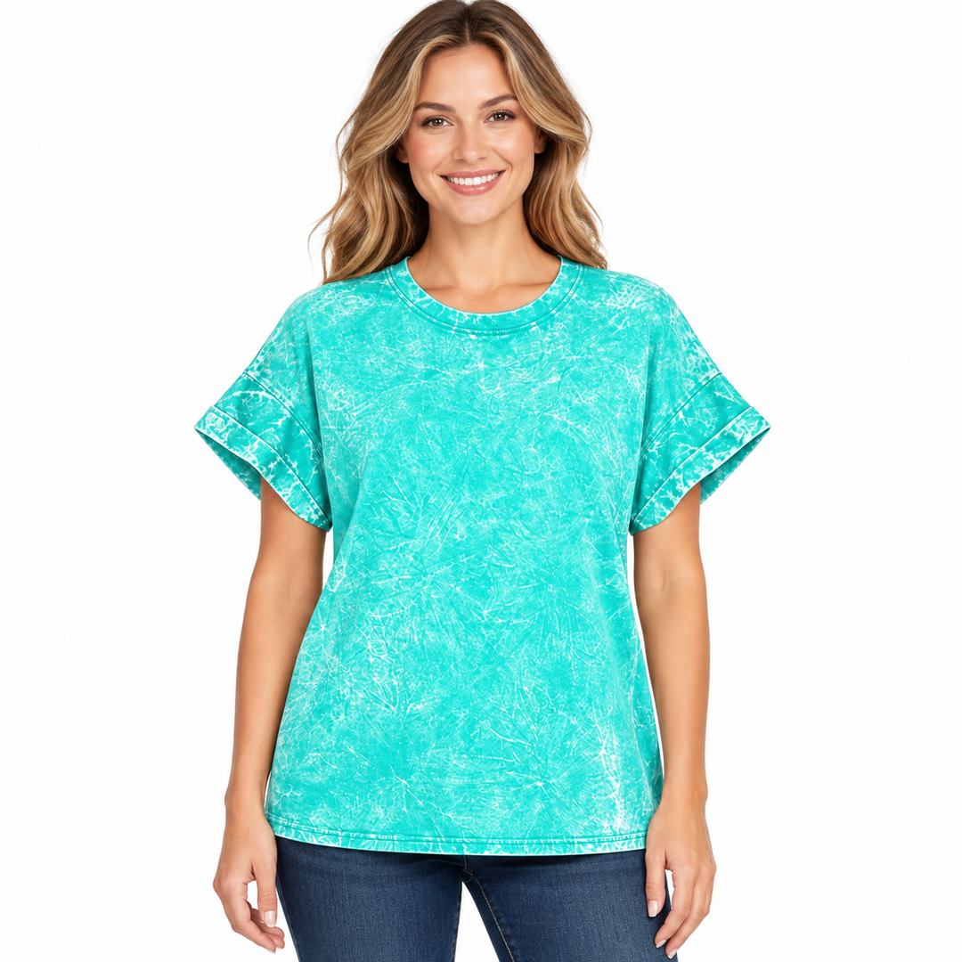 A woman modeling a short-sleeve crewneck top with a turquoise and white mineral-wash pattern, paired with dark blue jeans, against a plain white background.