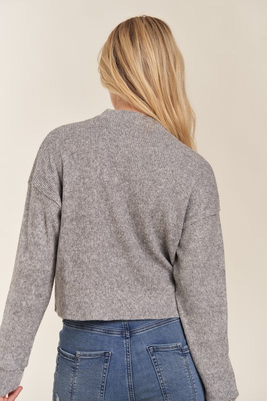 Person wearing a gray sweater and blue jeans on a beige background
