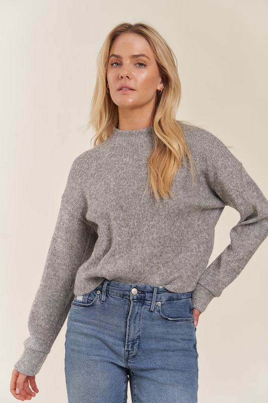 Woman wearing a gray sweater and blue jeans against a beige background