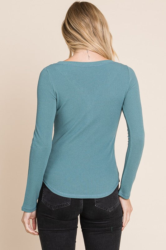 Person wearing a teal long-sleeve top against a beige background
