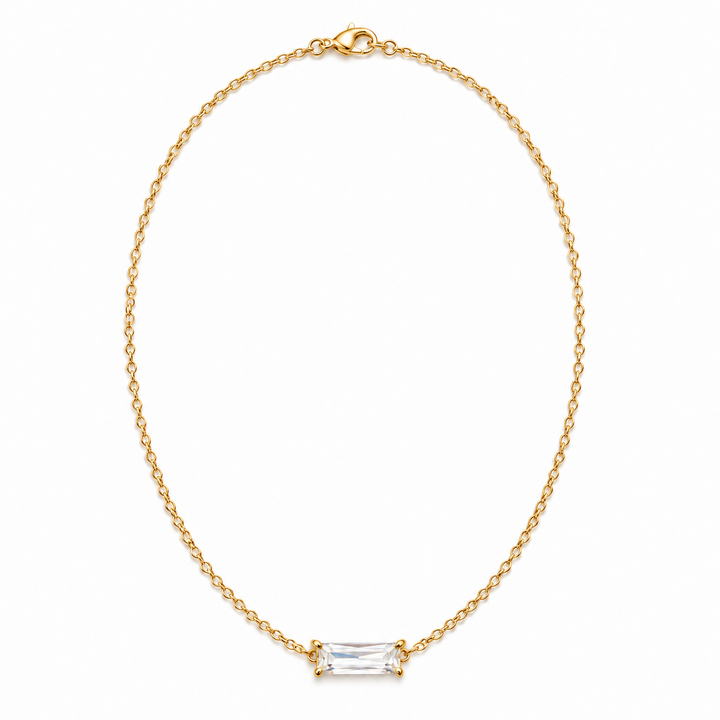A delicate gold chain necklace with a small rectangular clear baguette-cut gemstone pendant, displayed on a clean white background.