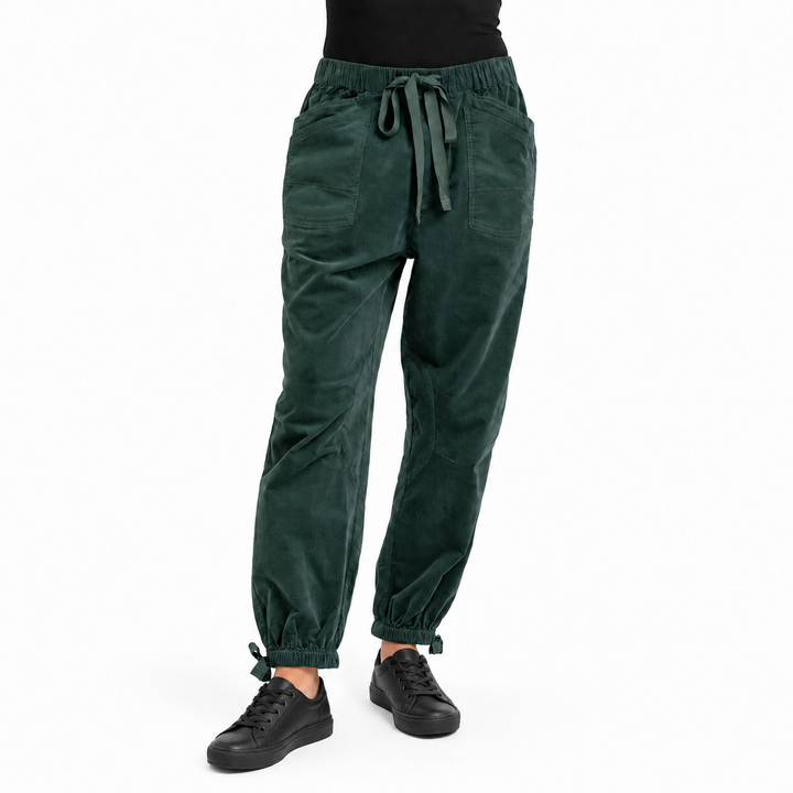 A person wearing dark green corduroy jogger pants with an elastic drawstring waist and elastic cuffs, paired with black sneakers against a plain white background.