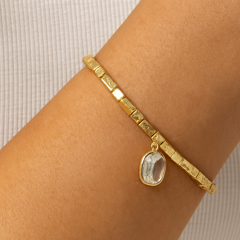 Gold bracelet with a pendant on a wrist against a neutral background