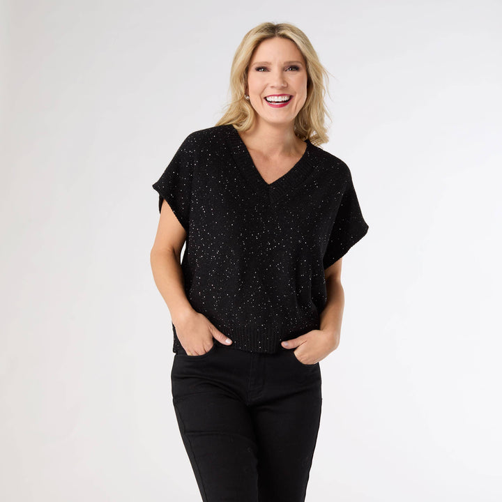 Woman wearing a black speckled top and black pants on a white background