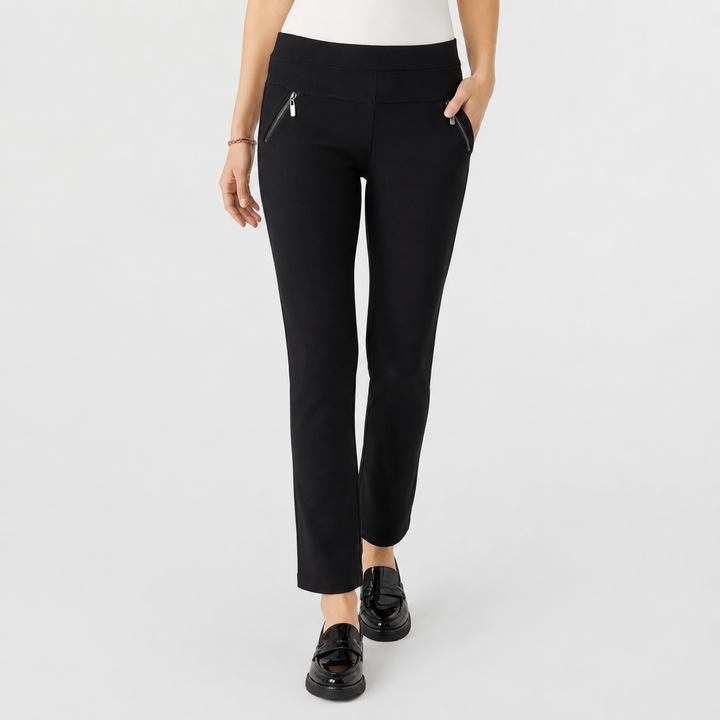 A model wearing black ankle-length pants with diagonal zippered pockets, paired with black loafers, shown against a light gray studio background.