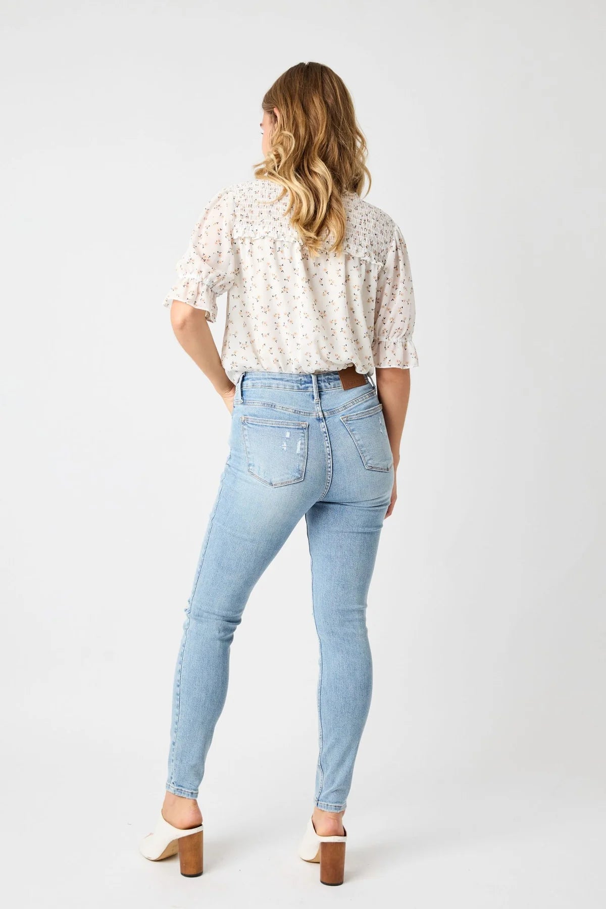 Woman wearing light blue jeans and a white floral blouse on a white background