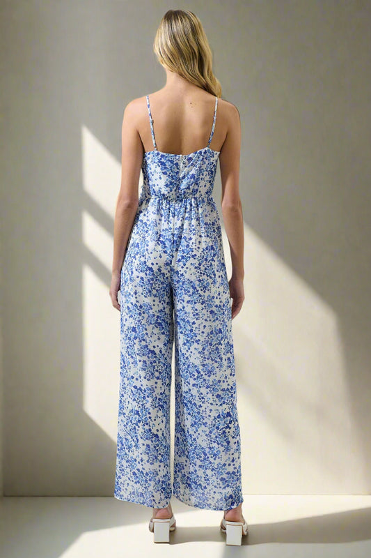 Woman wearing a blue floral jumpsuit on a plain background