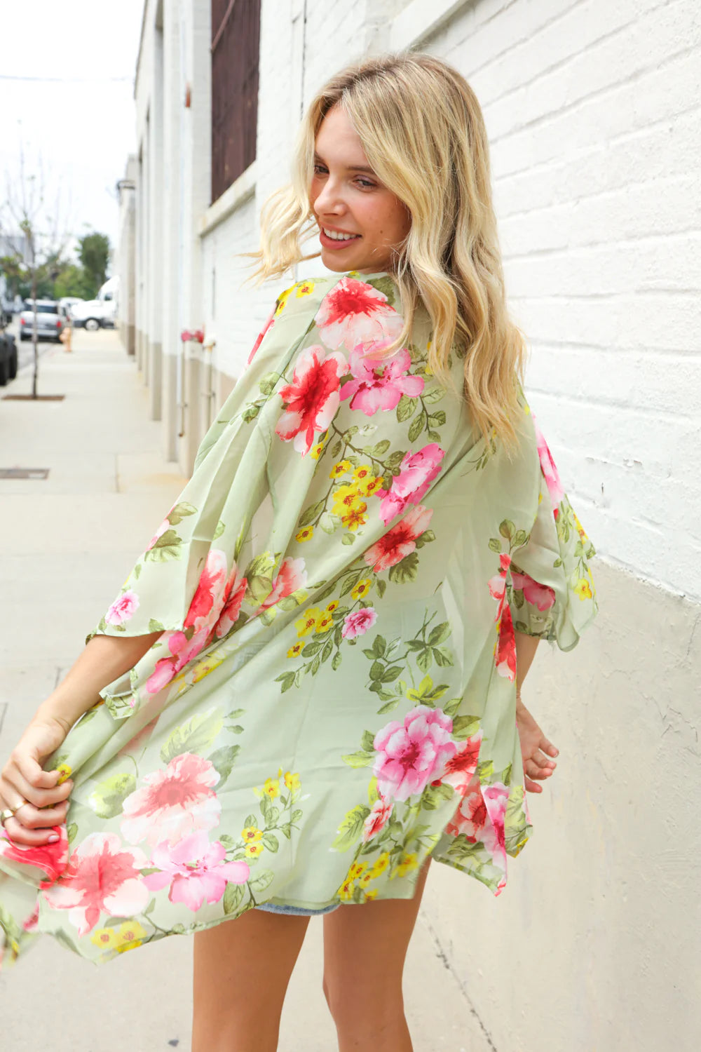 Woman wearing a floral dress standing against a white wall.