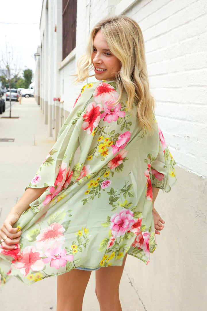 Woman wearing a floral dress standing against a white wall.