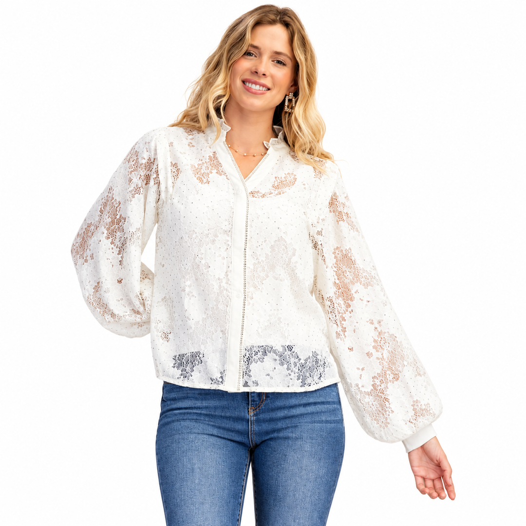 A woman modeling a white sequined jacket with sheer lace sleeves and blue jeans against a plain white background.
