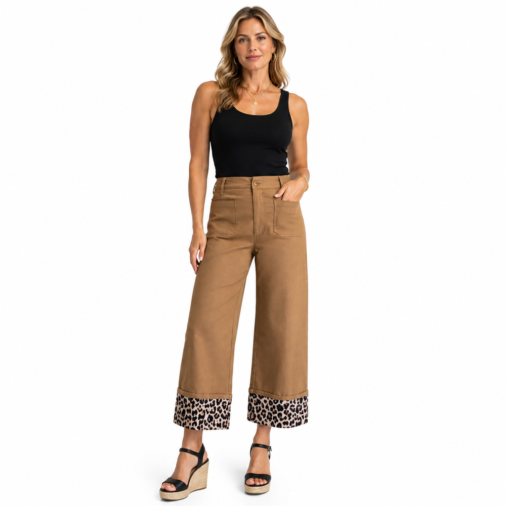 A woman modeling a pair of high-waisted, wide-leg cropped pants in tan, featuring a leopard-print patterned cuff and a black ribbed tank top, against a plain white background.